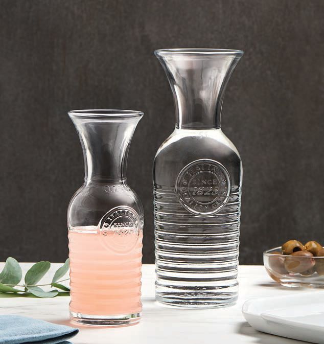 Due caraffe di vetro trasparente, una con un liquido rosa, su un tavolo con foglie e piatti.