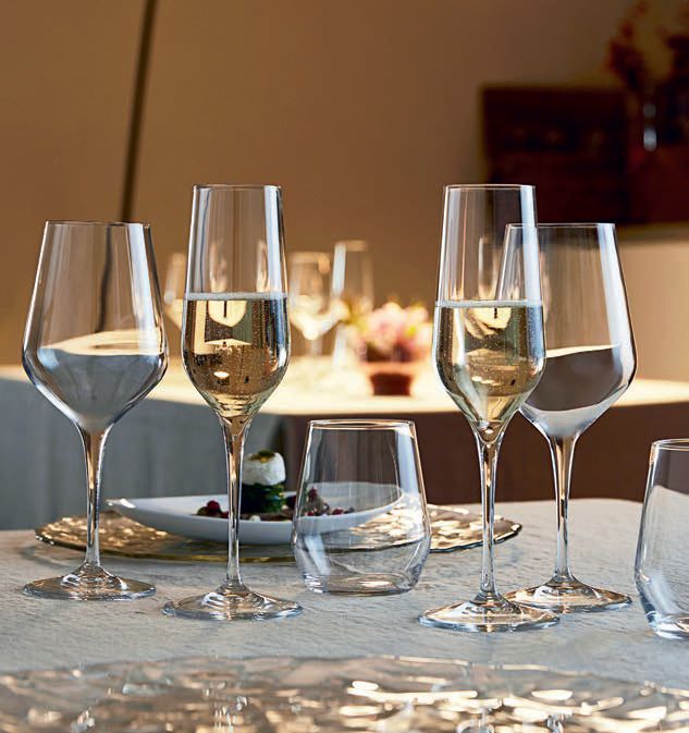 Quattro bicchieri da vino e un bicchiere d'acqua disposti su un tavolo da pranzo in un ristorante illuminato da luci soffuse.