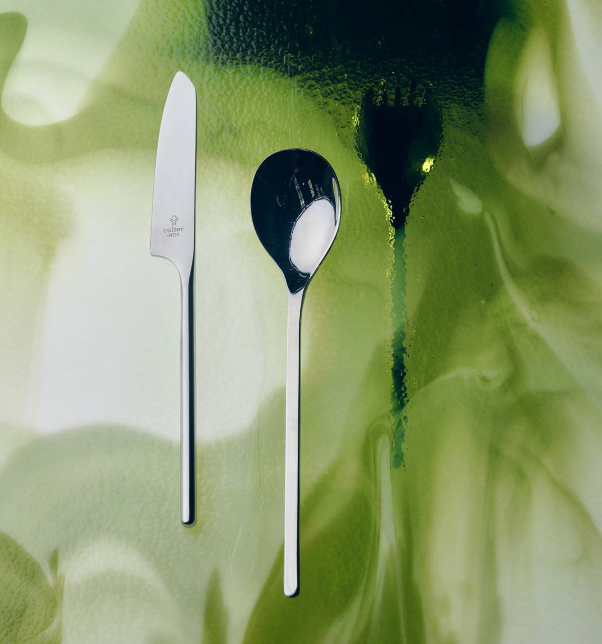 Coltello e cucchiaio d'argento su uno sfondo astratto verde.