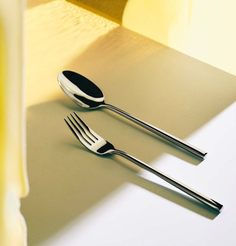 Un cucchiaio e una forchetta su un tavolo illuminato dal sole, che proiettano ombre morbide.