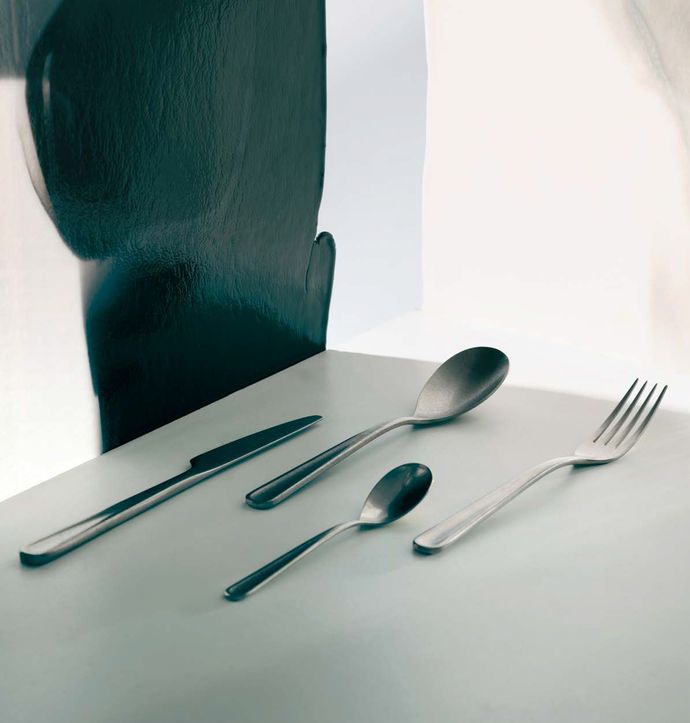 Tavola apparecchiata con coltello, cucchiaio e forchetta su un tavolo bianco accanto a una sedia scura.
