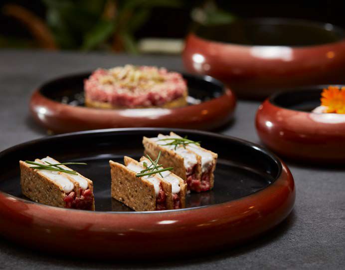 Tre antipasti gourmet serviti su piatti scuri, con guarnizioni e ciotole sfocate sullo sfondo.