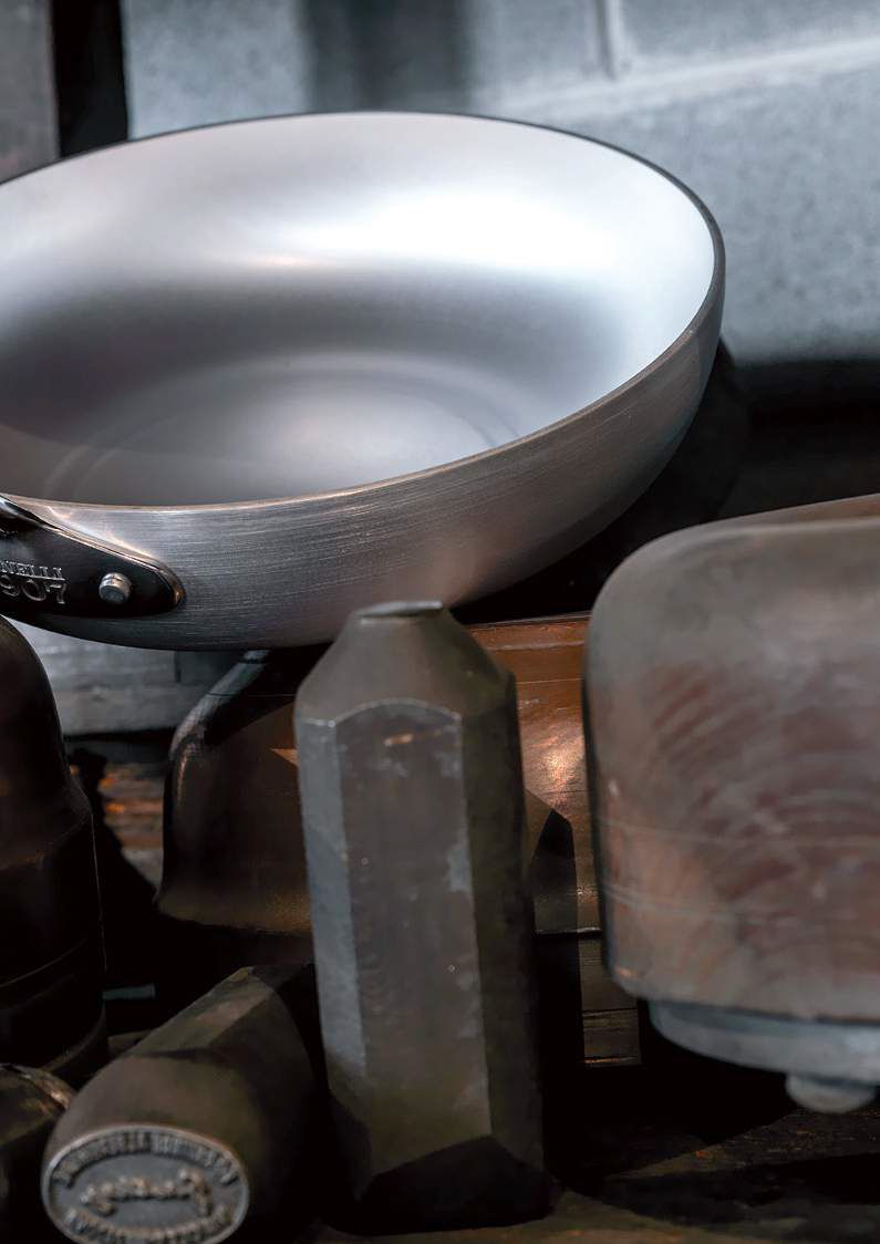 Wok argentato e utensili da cucina scuri su un piano di lavoro.