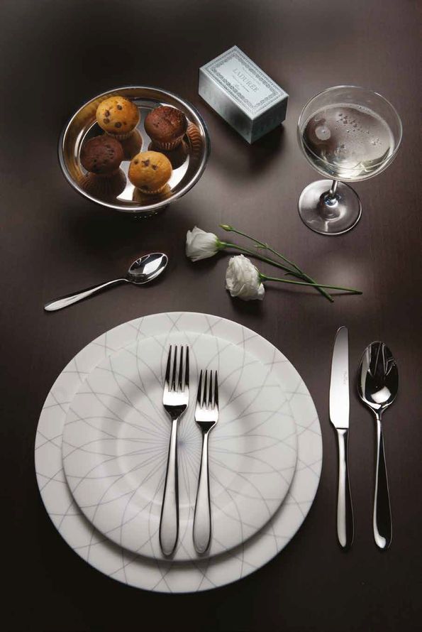 Tavola apparecchiata in modo formale con piatti, posate, rose bianche, cioccolatini e un calice di champagne.