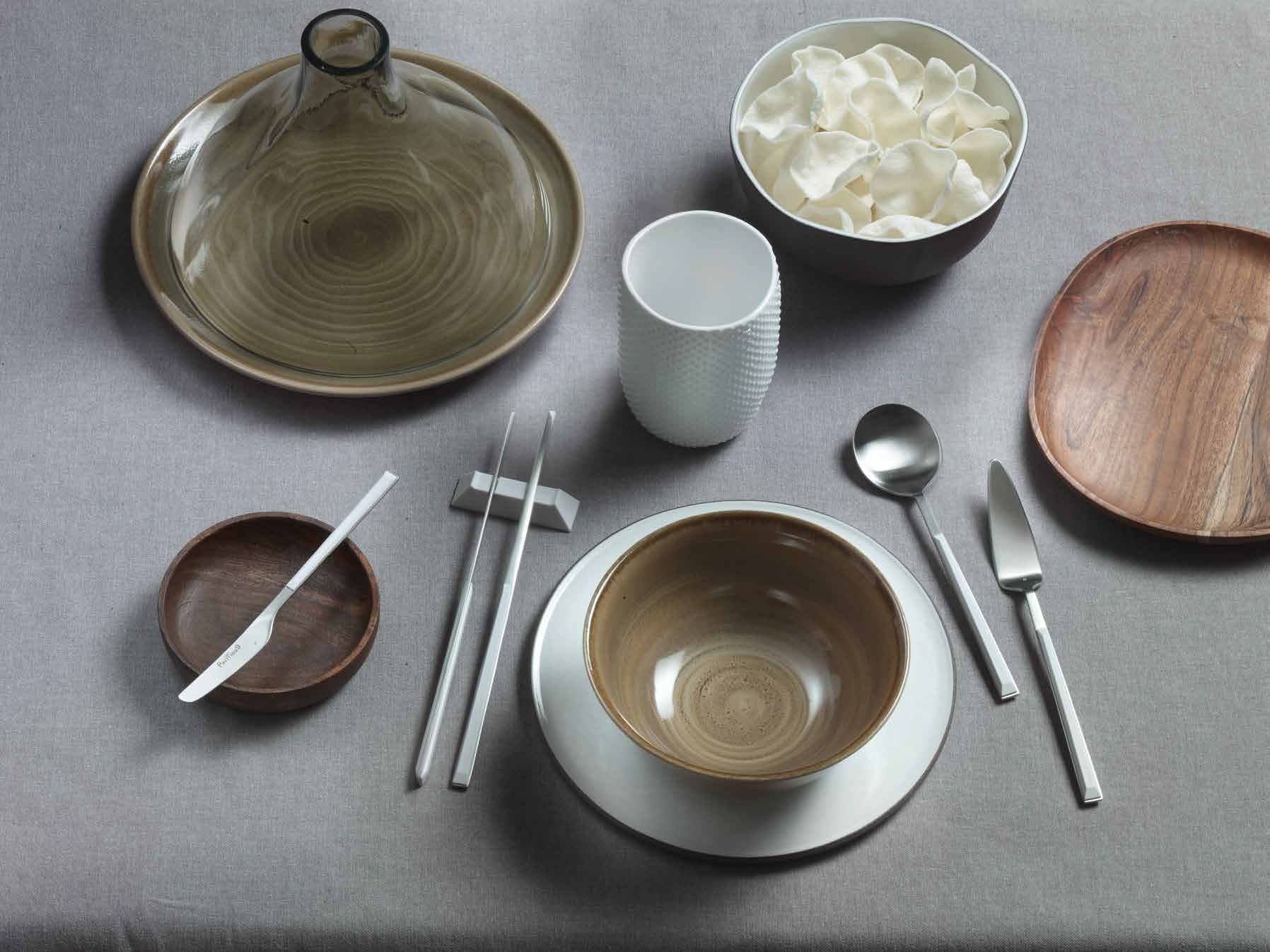 Assortimento di ciotole, piatti, tazze e utensili in ceramica disposti su una superficie grigia