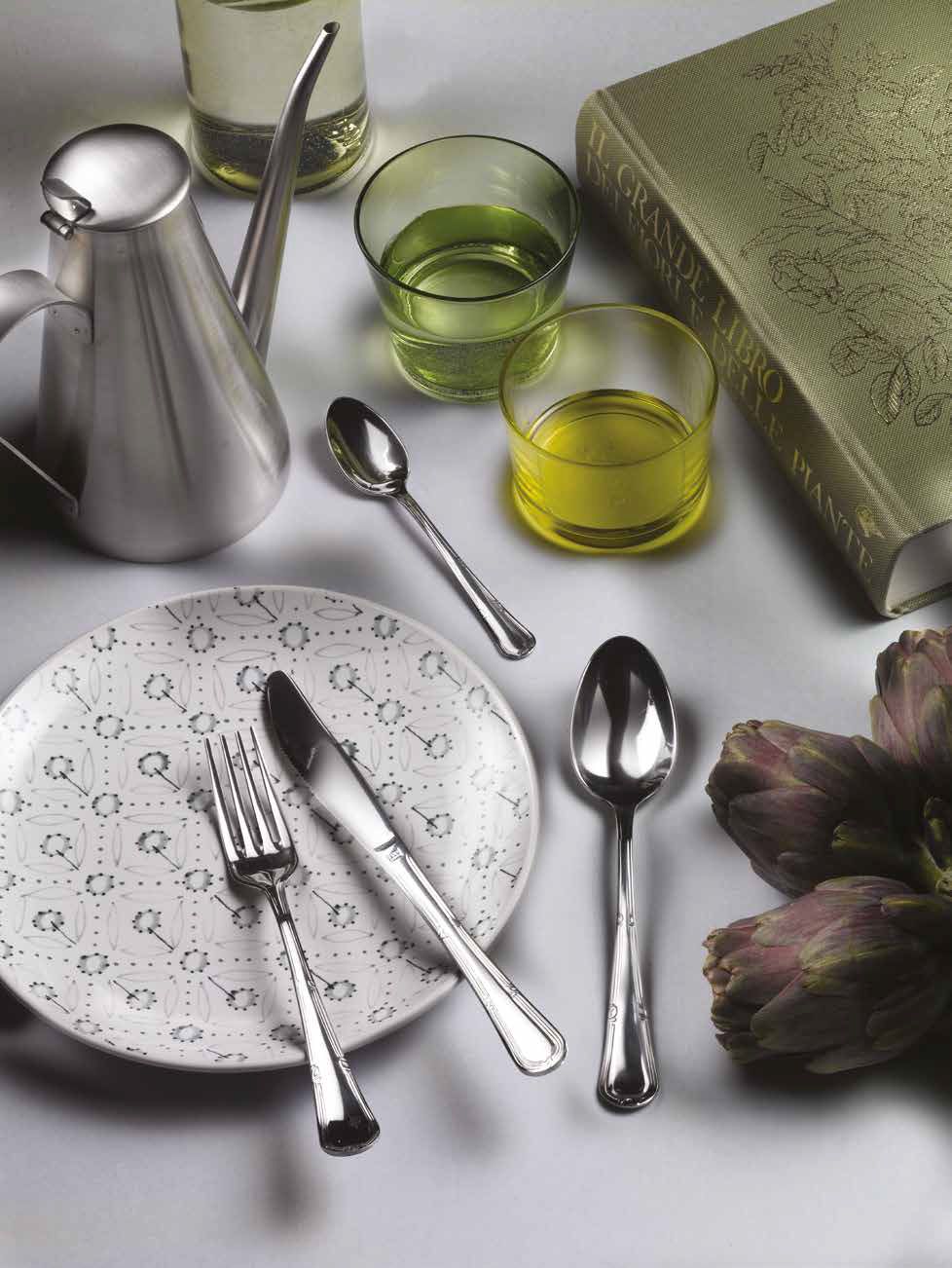Posate d'argento, piatto decorato, bicchieri verdi e gialli e carciofi su un tavolo chiaro.