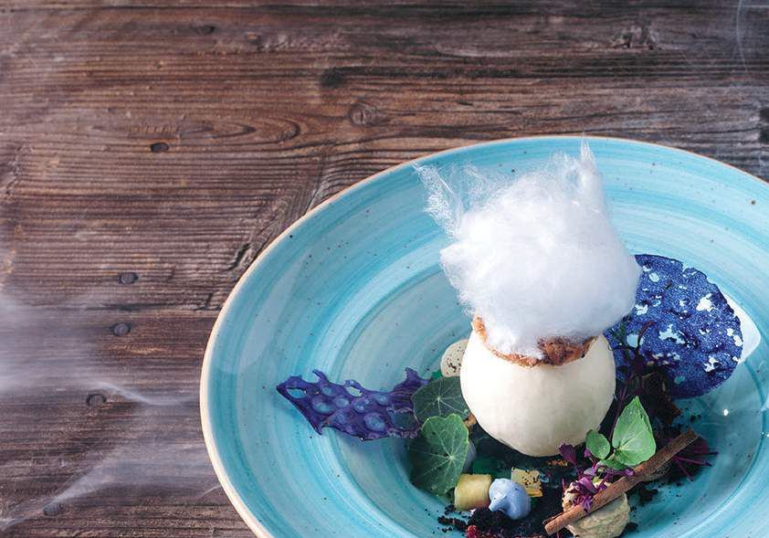 Dessert guarnito con zucchero filato su un piatto blu appoggiato su un tavolo di legno.