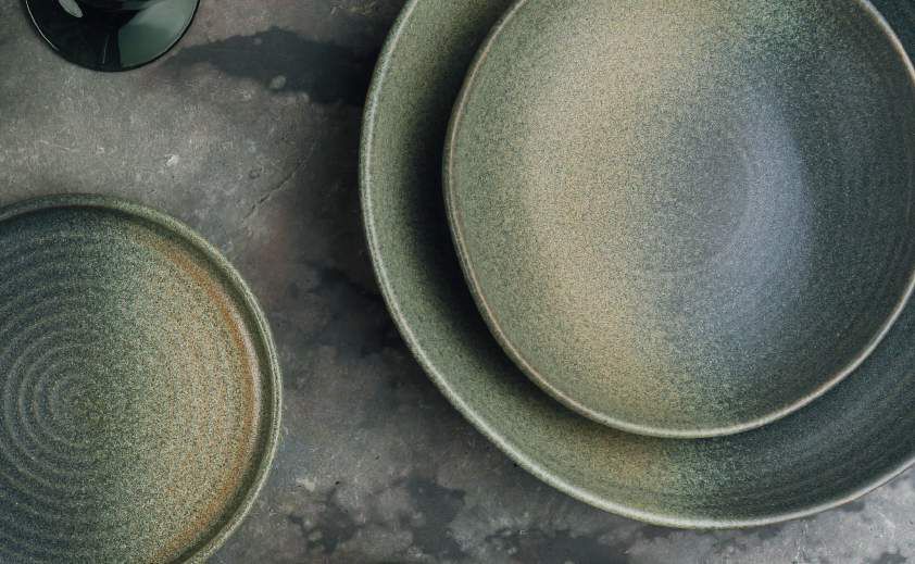Piatti di ceramica verde impilati su una superficie scura e ruvida.