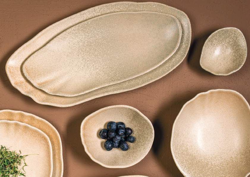 Piatti assortiti color crema e una piccola ciotola di frutti di bosco scuri su uno sfondo beige.