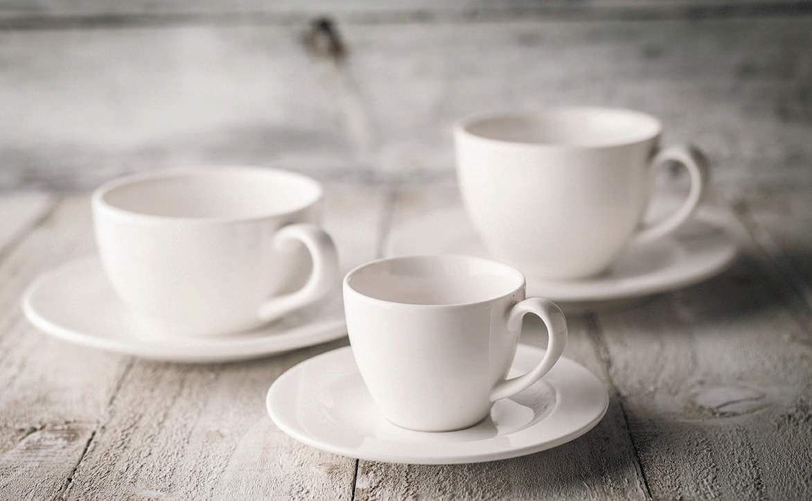 Tre tazze da caffè bianche su piattini, appoggiate su un tavolo di legno rustico.
