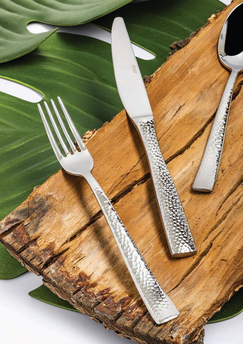Tre utensili d'argento su una tavola di legno rustica su uno sfondo di foglie verdi.