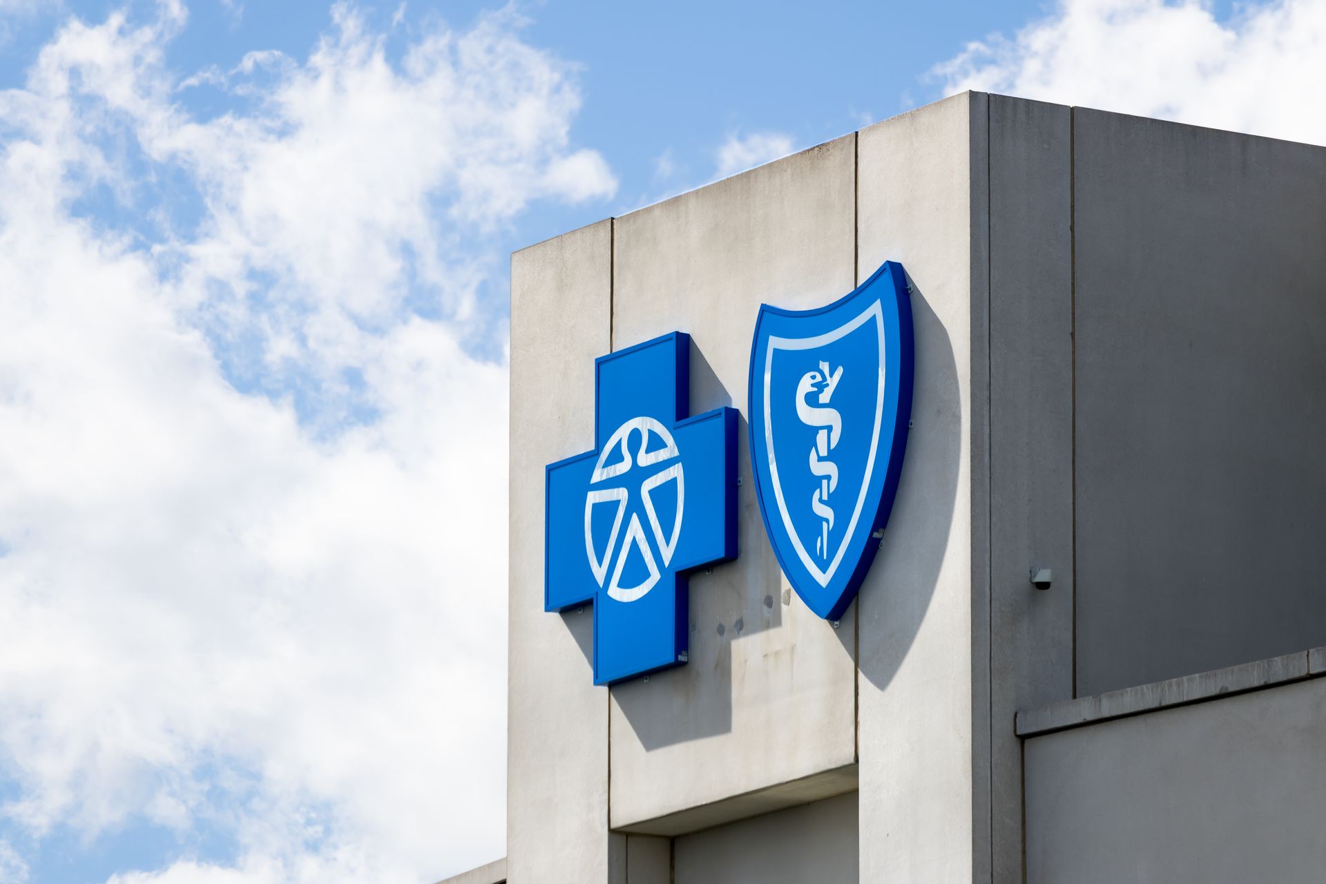 Blue health insurance logos on a gray building against a cloudy sky