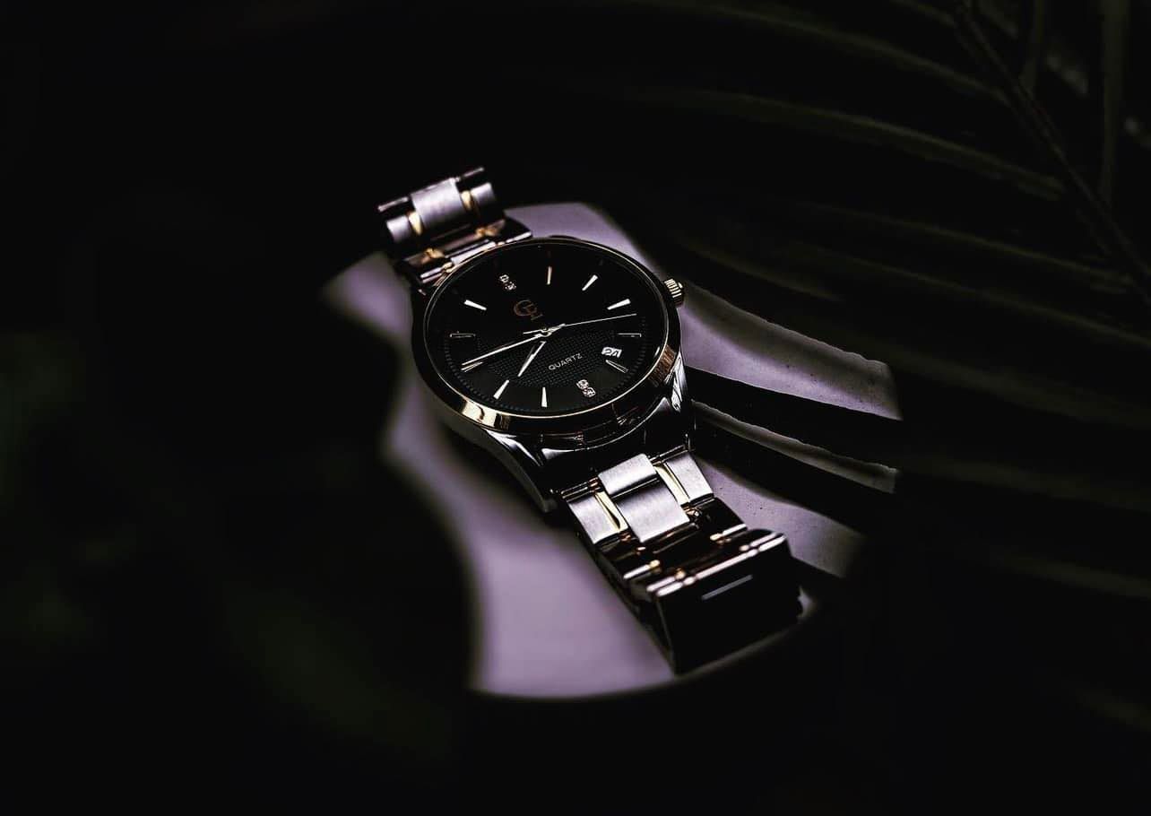 Gold wristwatch on a reflective surface with a dark background and foliage.
