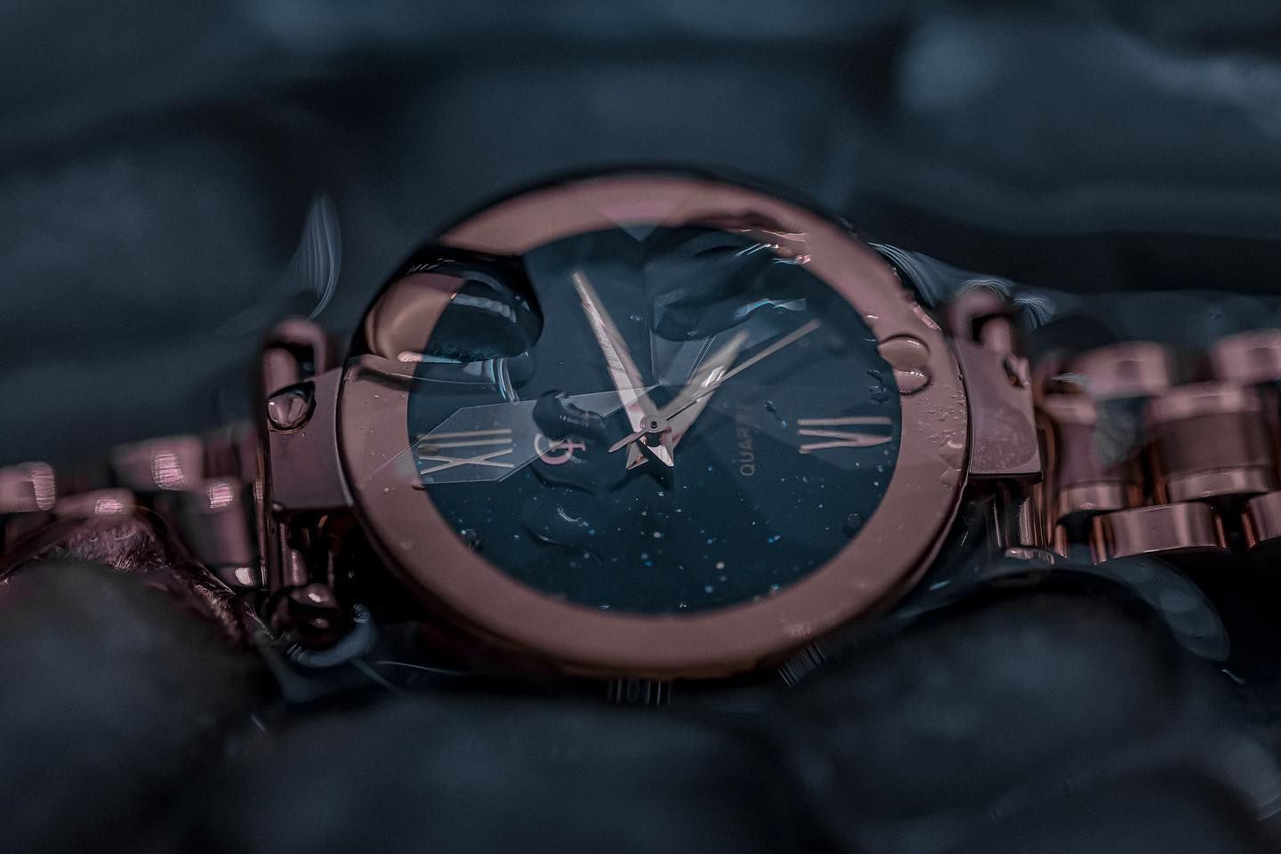 Rose gold wristwatch on a dark, textured surface, the watch face displays the time.