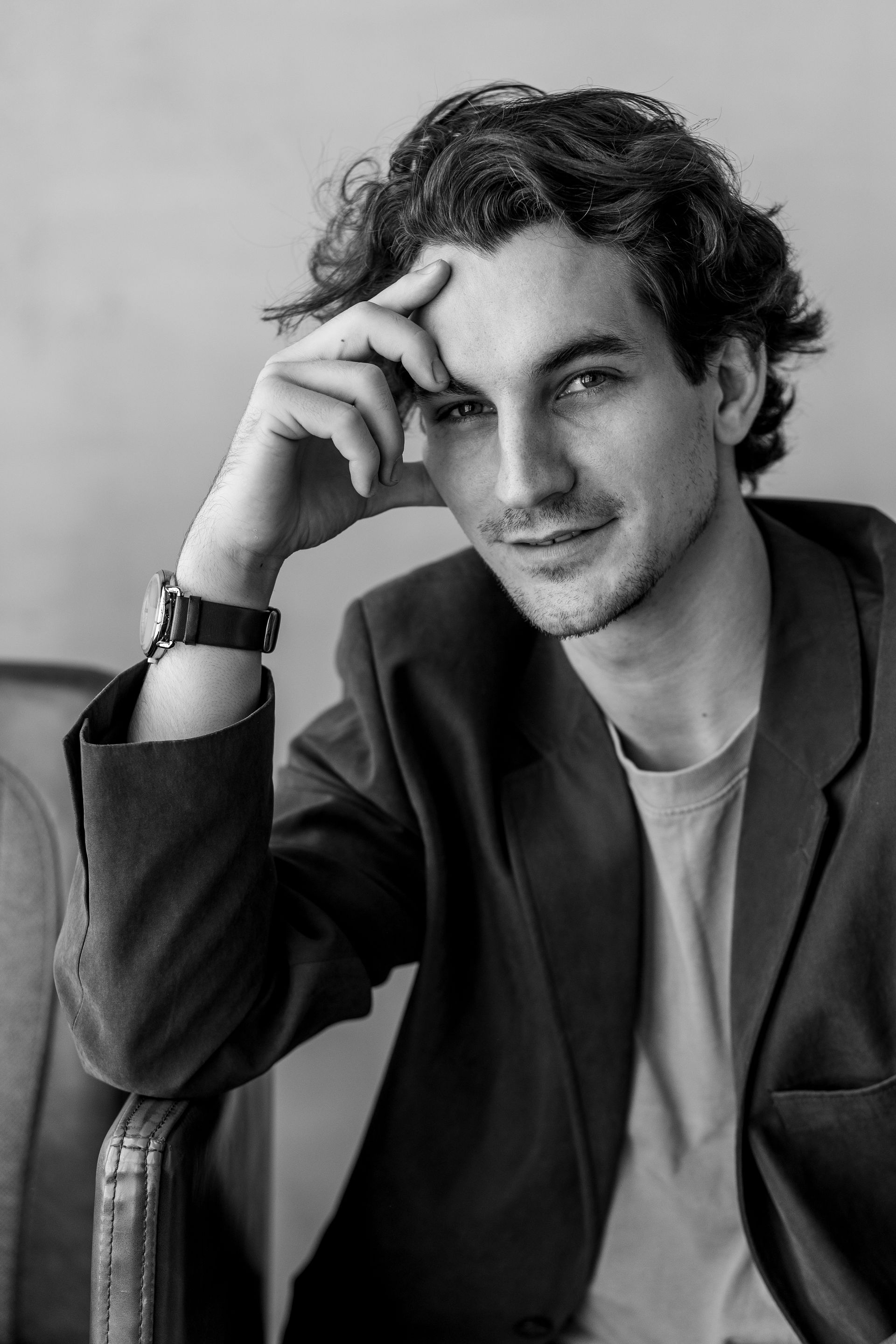 Man in blazer resting hand on forehead, looking at the camera.
