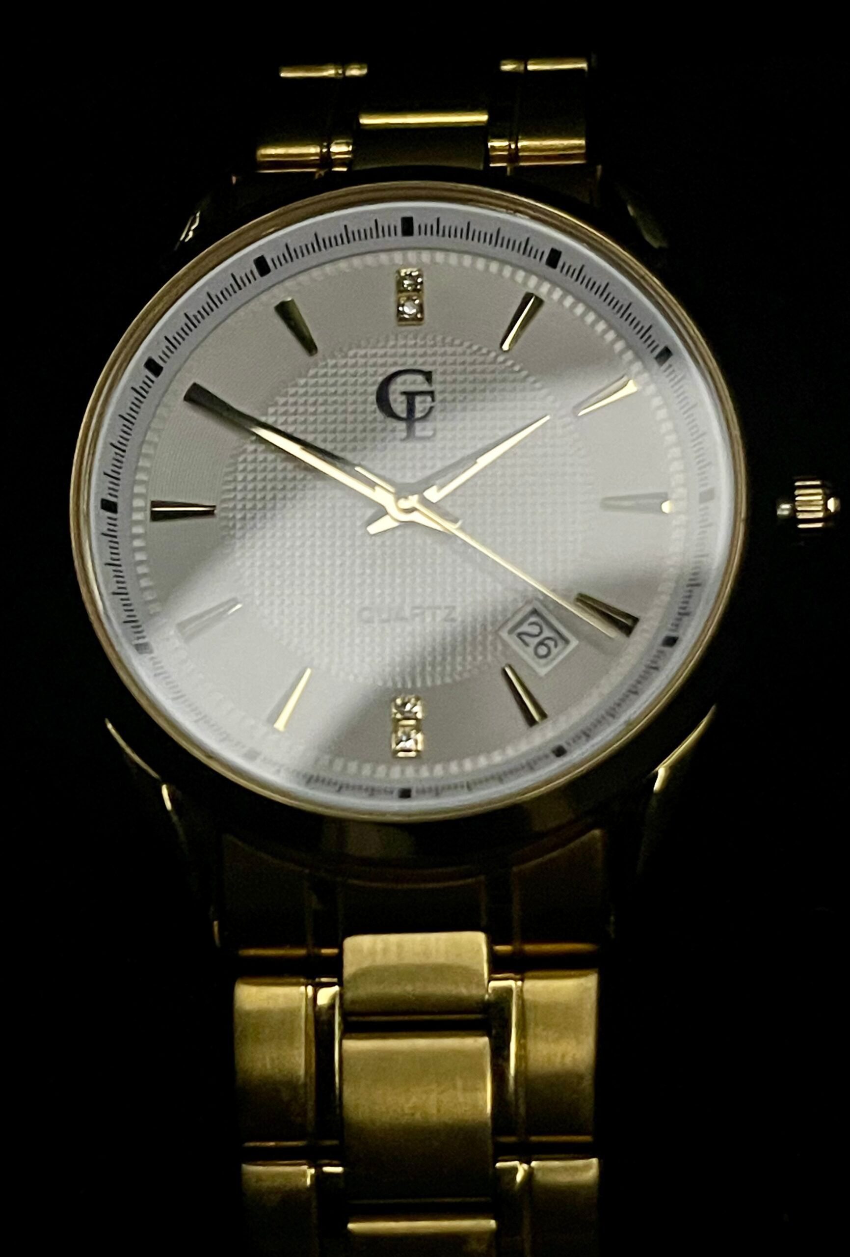 Gold wristwatch with a light-colored face and date window on a black background.