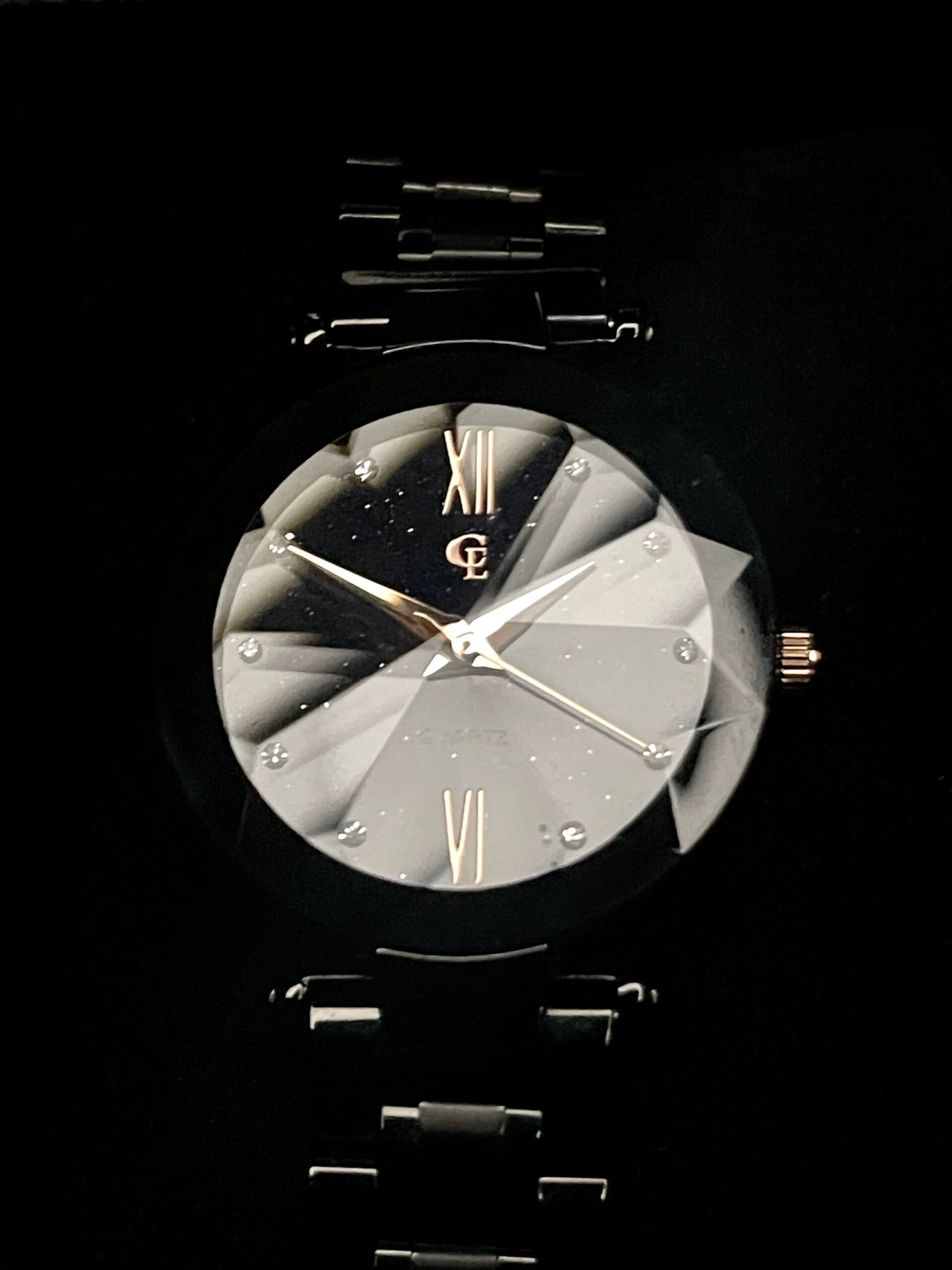 Black wristwatch with diamond-faceted face and Roman numeral hour markers, set against a dark background.
