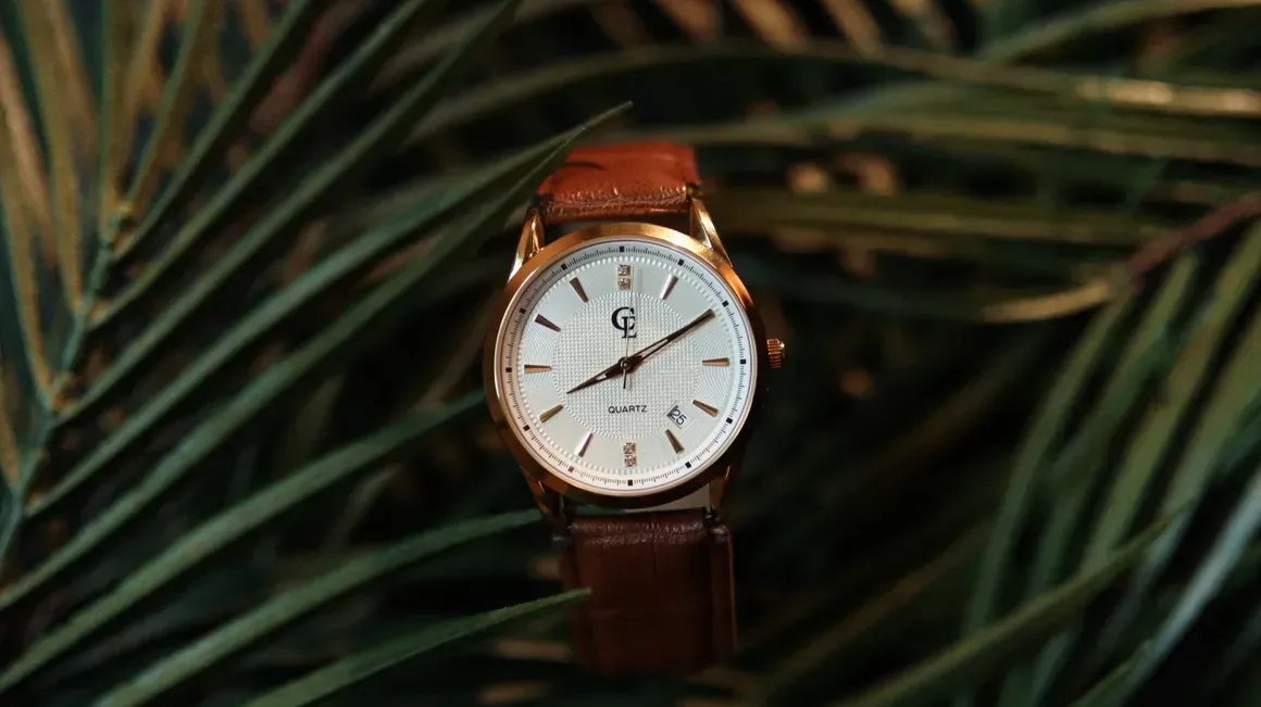 Gold wristwatch with brown leather band, on a bed of green palm leaves.
