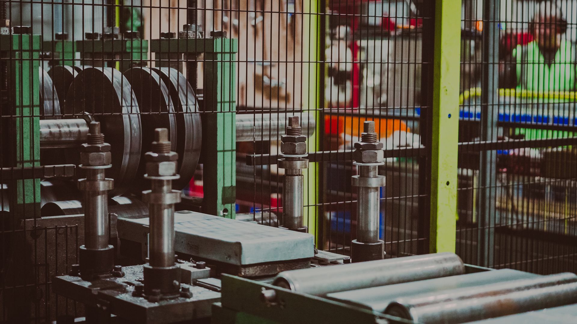 Industrial machinery in a factory, rolling steel beams. Workers in background.