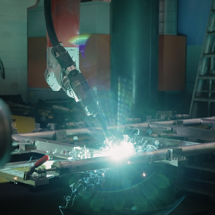 Welding robot in action, bright blue light, sparks, industrial setting.