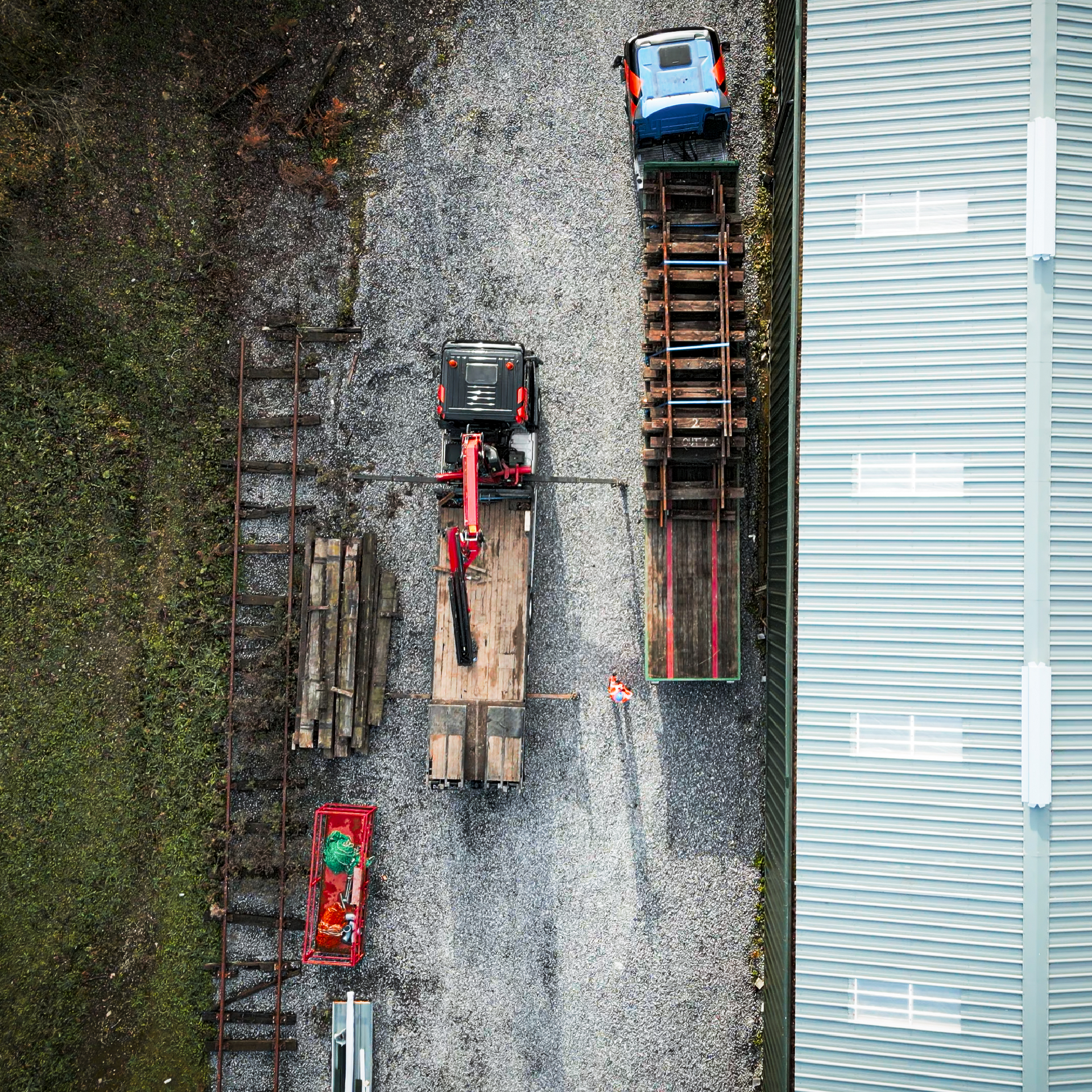 Overhead view of railway construction with trucks, equipment, and workers, gray gravel area.