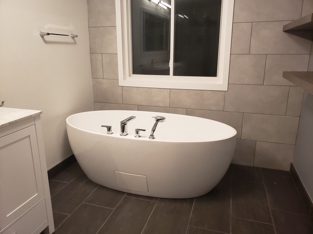 A white bathtub in a bathroom next to a window