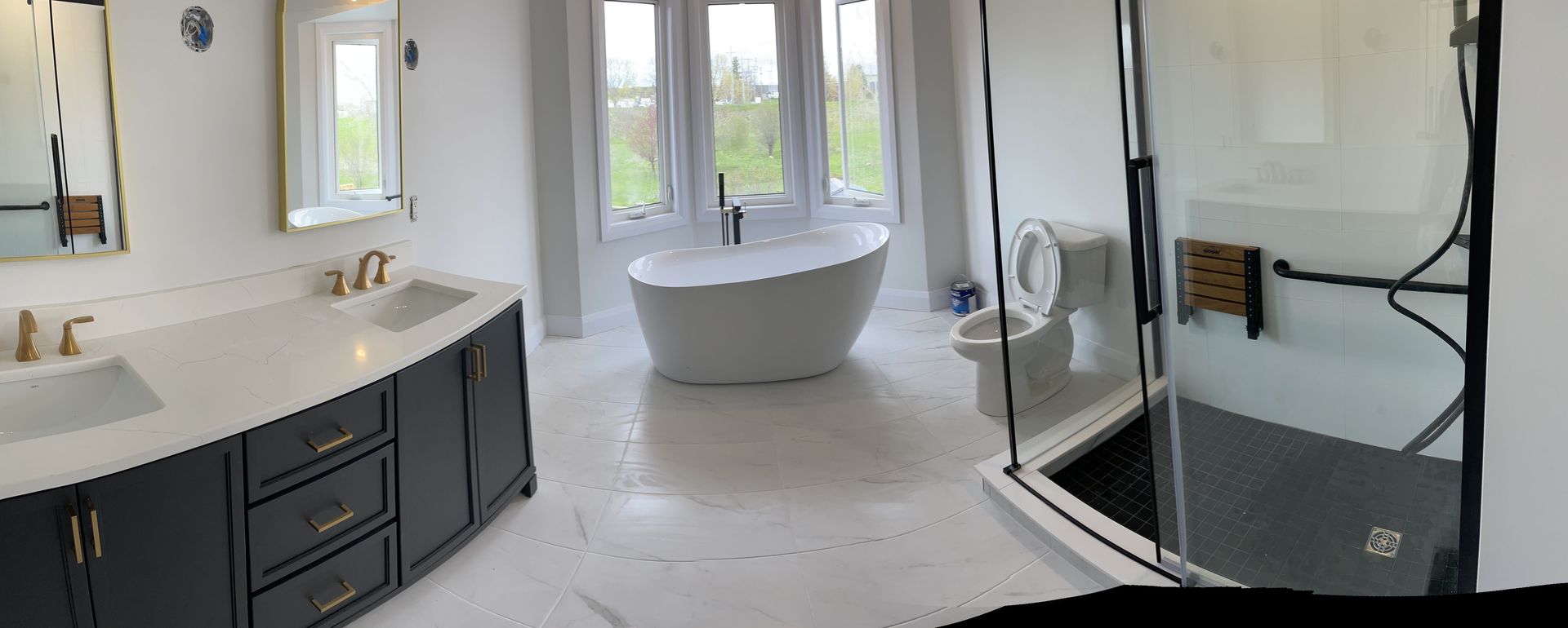 Bathroom with white walls, black vanity, freestanding tub, glass shower, and large windows.