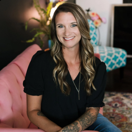 Woman with tattoos, smiling, sitting on pink couch in colorful room.