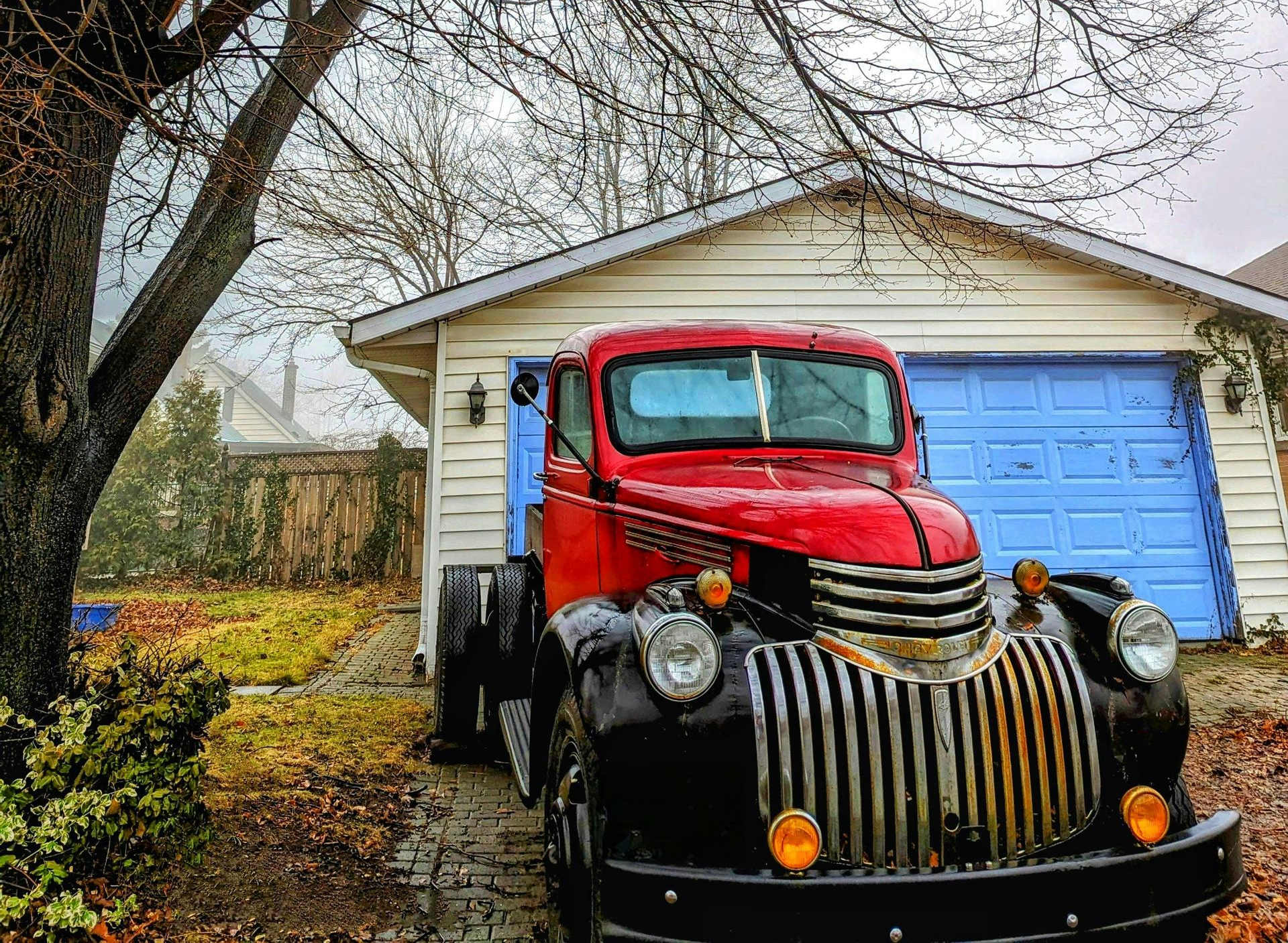 Red vintage truck parked in front of a blue garage on a cloudy day.