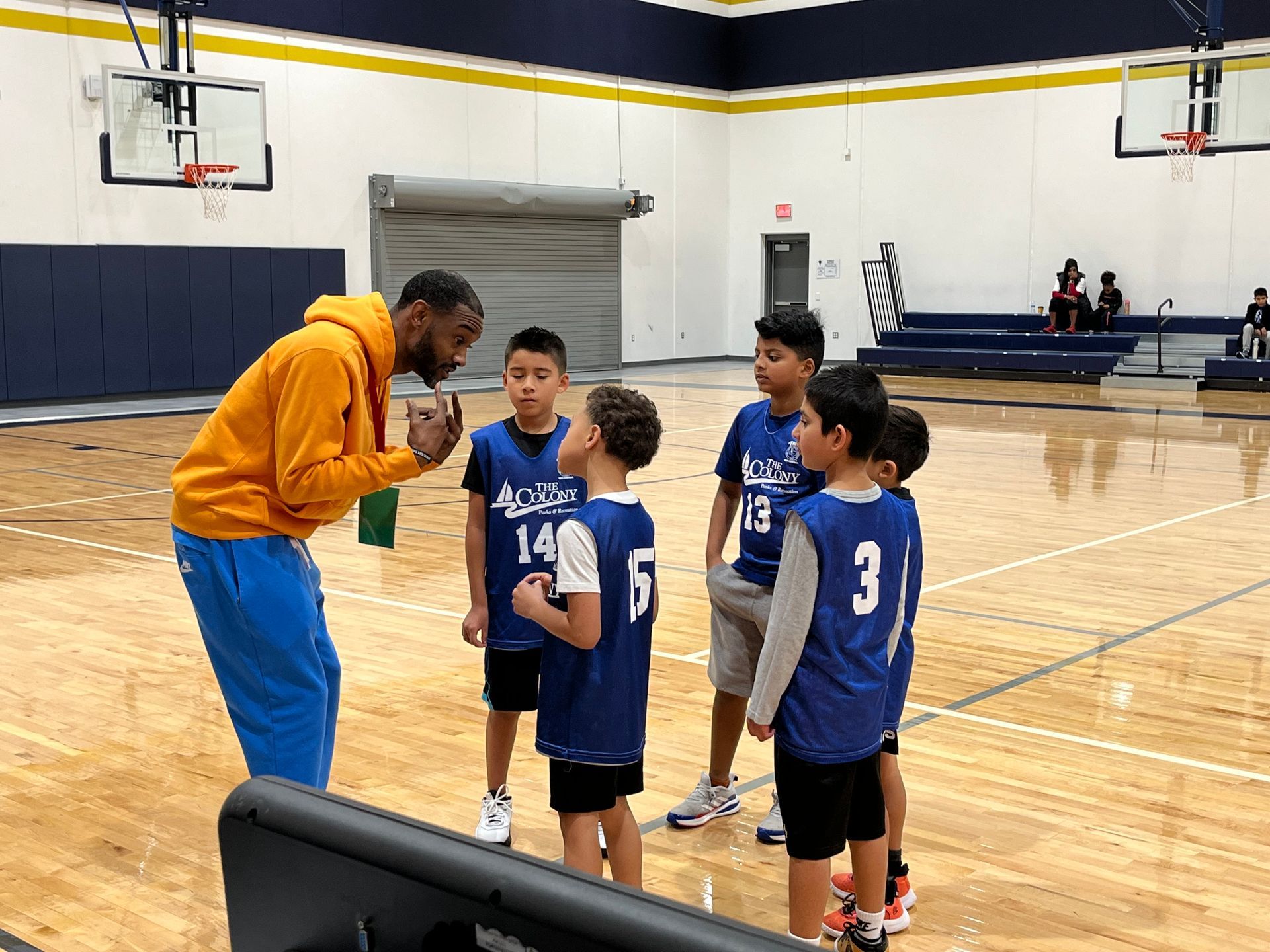A youth basketball team huddled around their coach as he gives them instruction. 