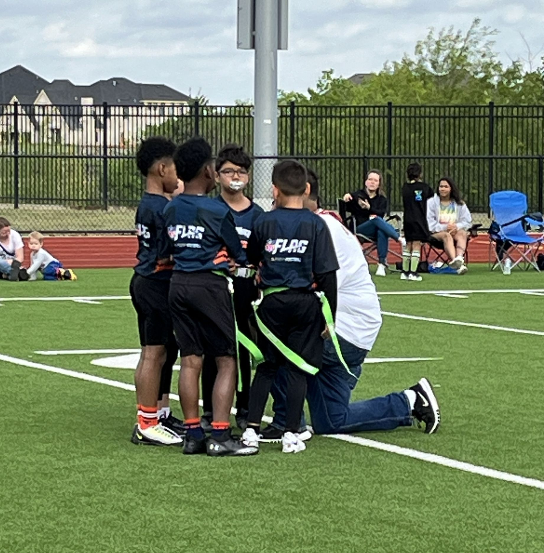 A NFL Flag football youth team huddled around their coach who is showing them the play. 