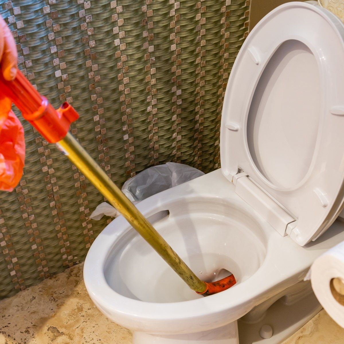 Toilet being plunged. Red and gold plunger in a white toilet bowl. Paper roll nearby.