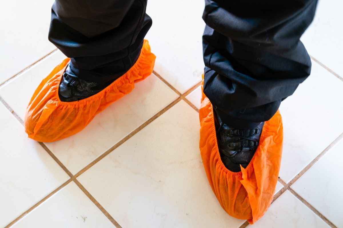 Person wearing black pants and orange shoe covers, standing on tiled floor.