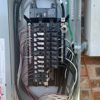 Electrical breaker panel with multiple black circuit breakers and exposed wiring inside a metal box