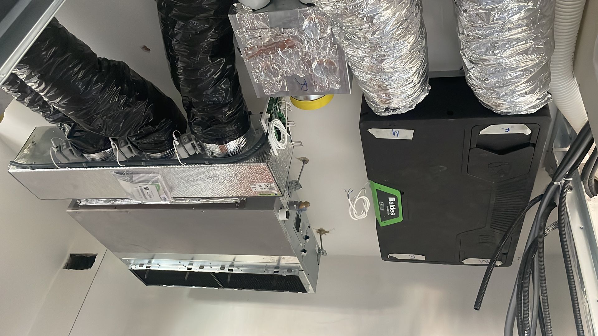 Condotti di ventilazione a soffitto, bocchette di aerazione e una scatola di derivazione nera in un locale tecnico.