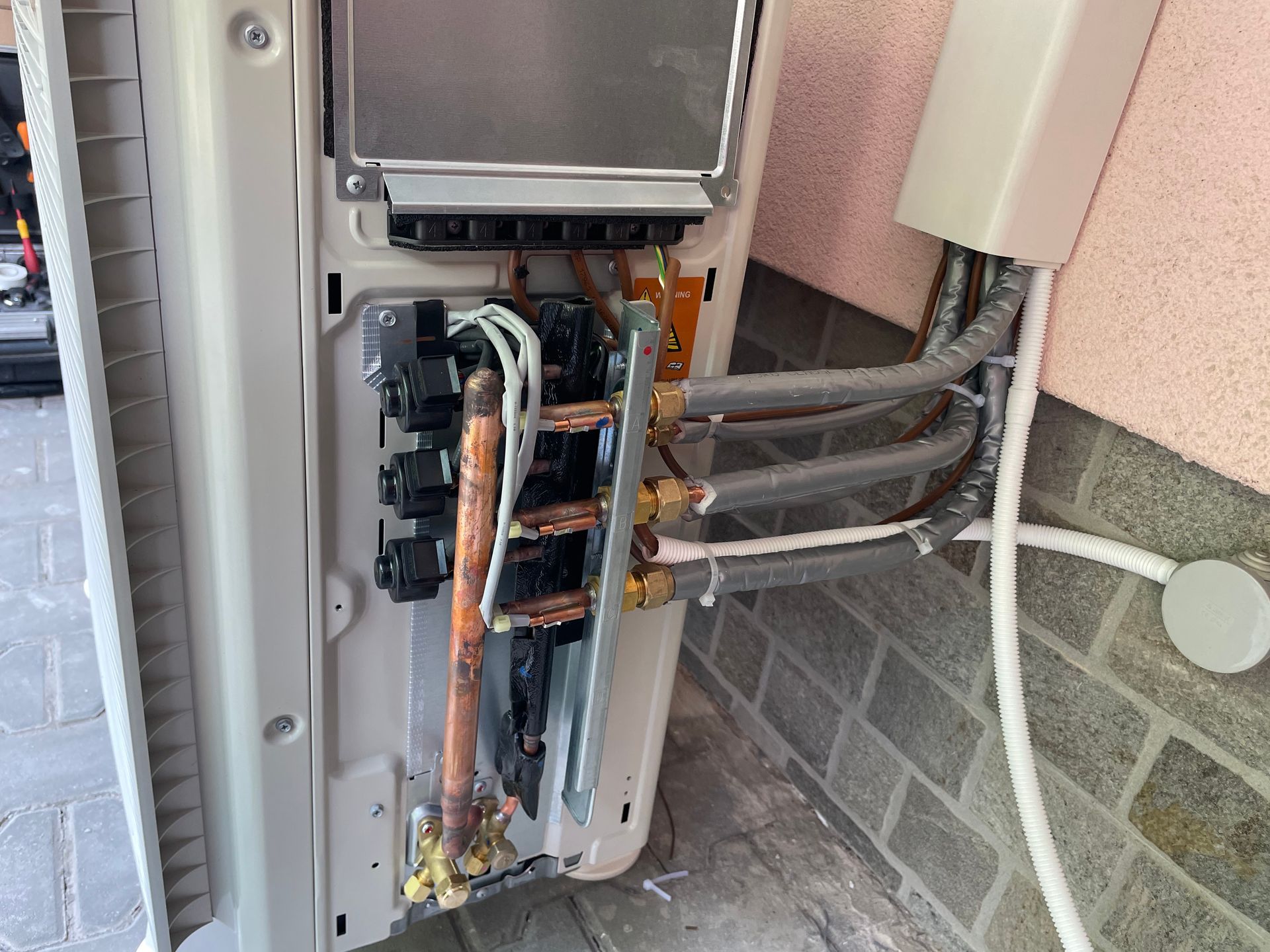 Quadro elettrico aperto con fili e tubi di rame a vista, montato su una parete esterna.