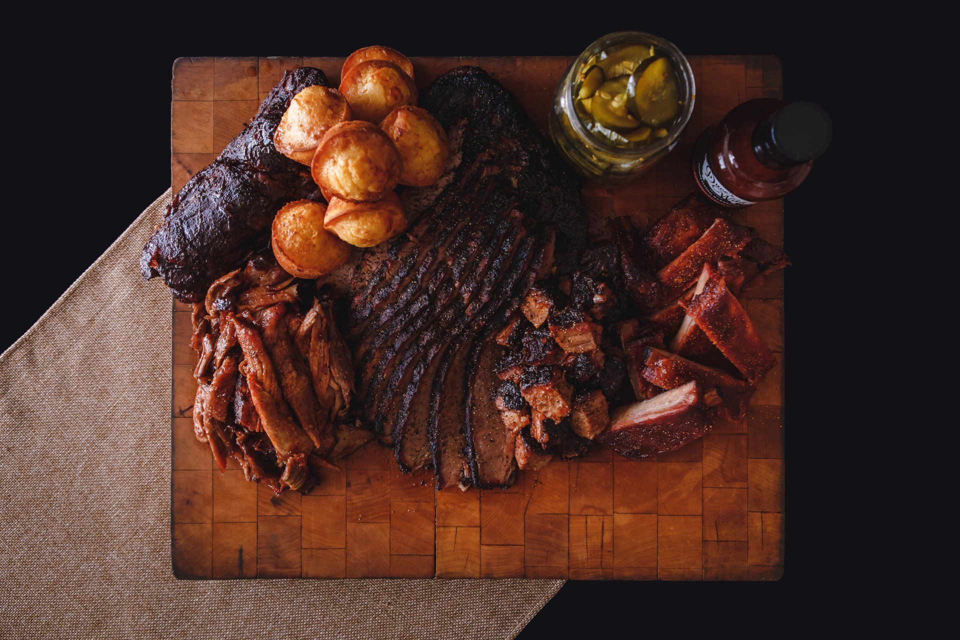 A wooden cutting board topped with meat , potatoes and pickles.