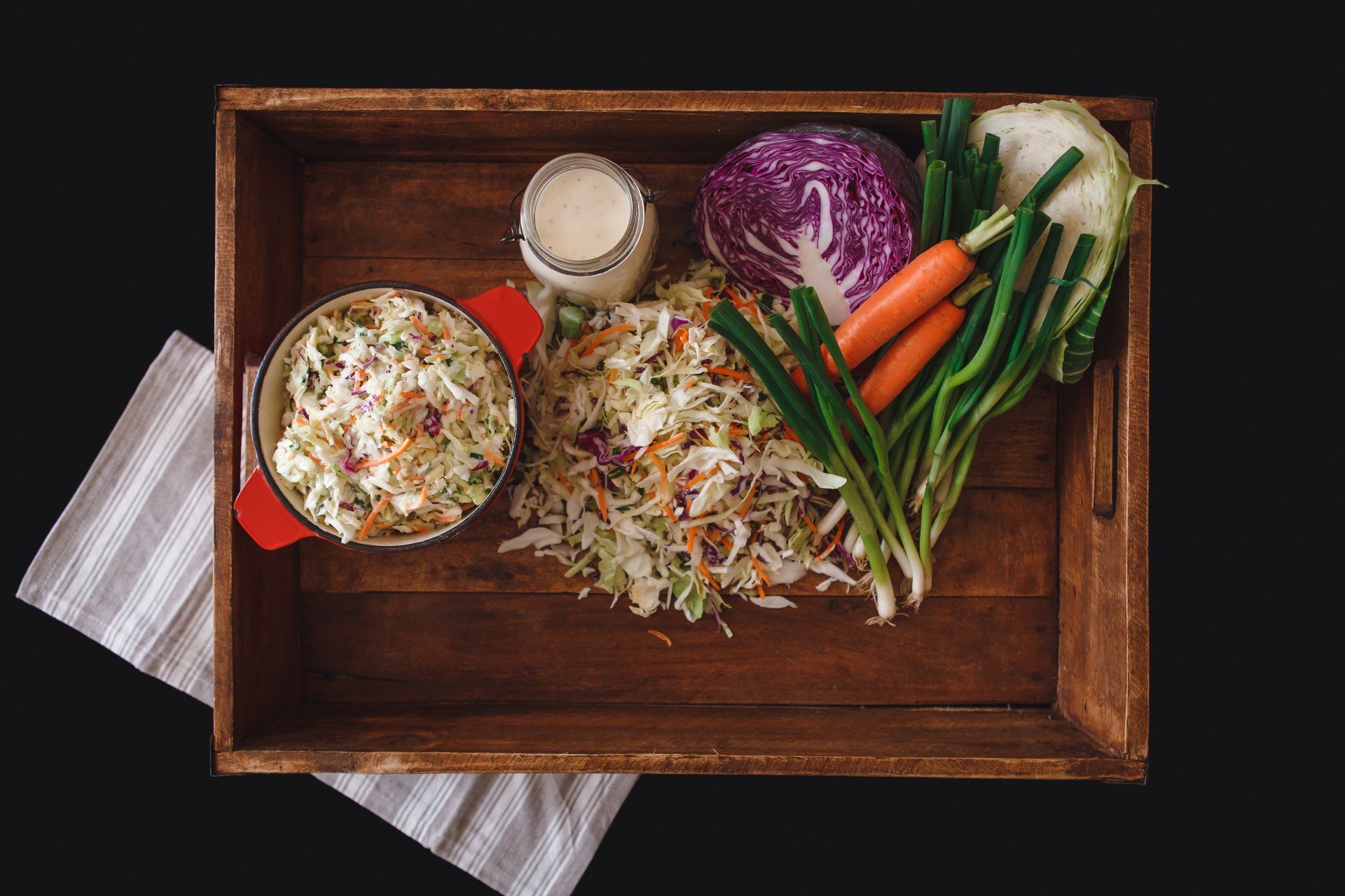 A wooden tray filled with coleslaw , carrots , cabbage and green onions.