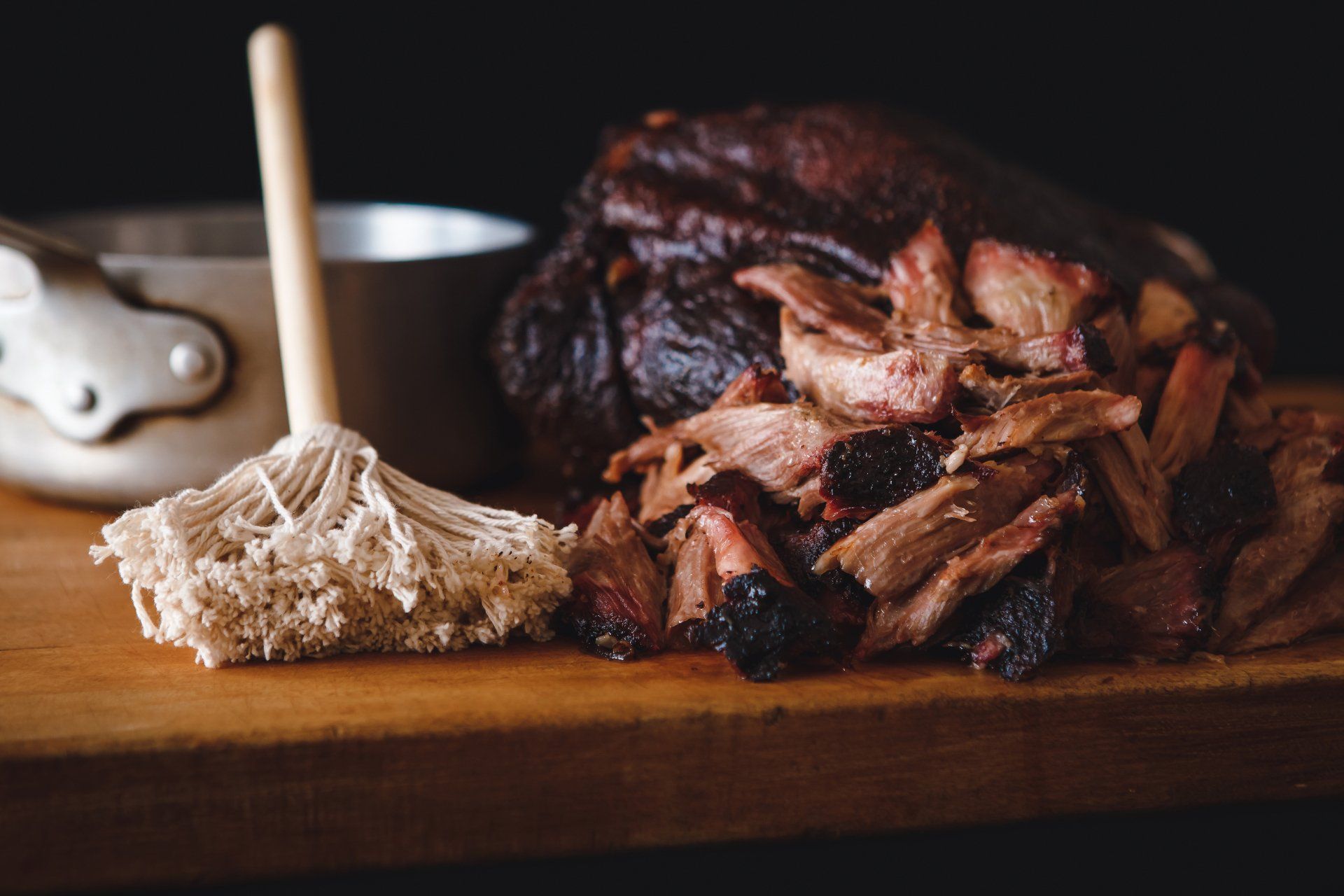 A pile of pulled pork is sitting on a wooden cutting board next to a mop.