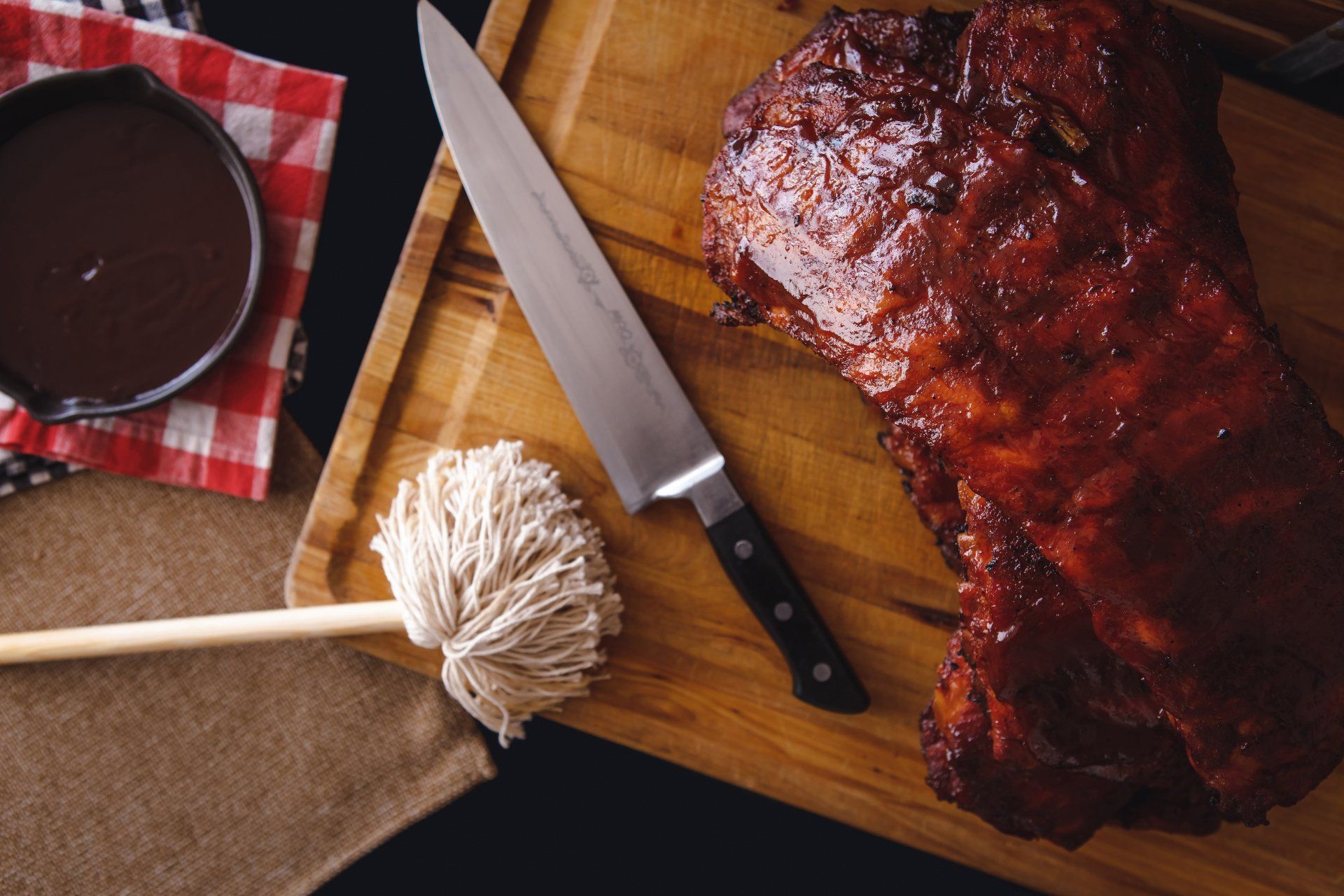 A cutting board with ribs sauce and a mop on it