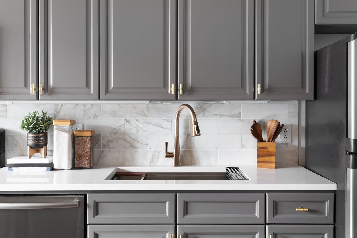 A kitchen with gray cabinets , stainless steel appliances , a sink , and a refrigerator.