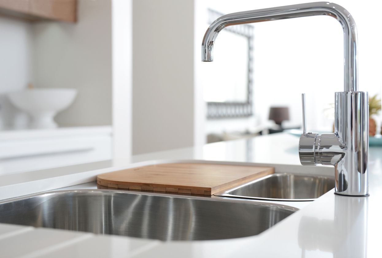 A kitchen sink with a faucet and a wooden cutting board on it.