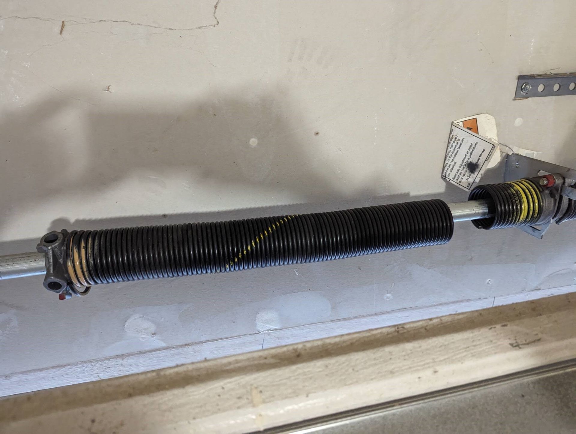Black garage door torsion spring on a metal rod, mounted above a garage door opening.