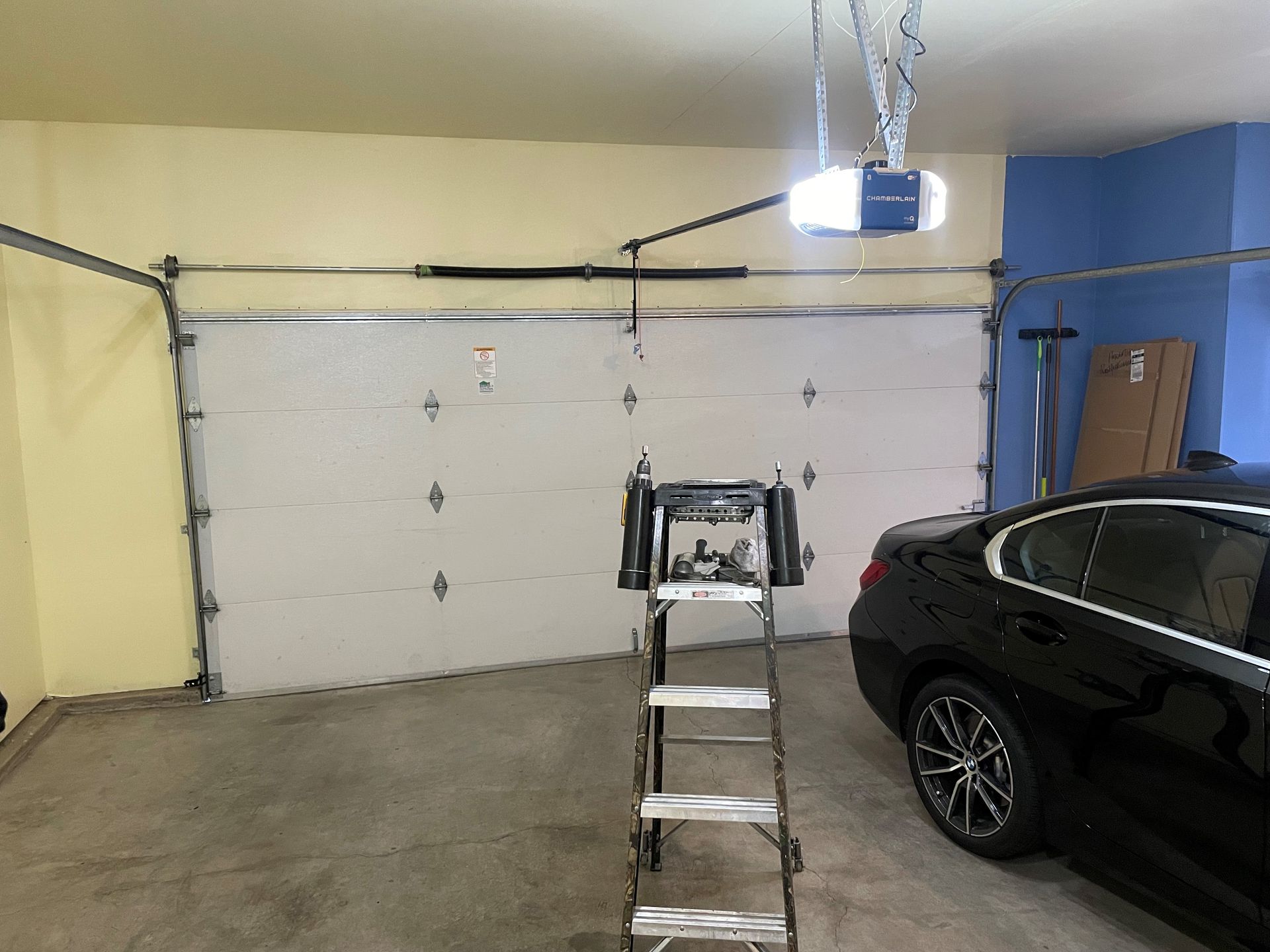 Garage interior with a car parked, ladder in front of a closed garage door and a garage door opener installed.