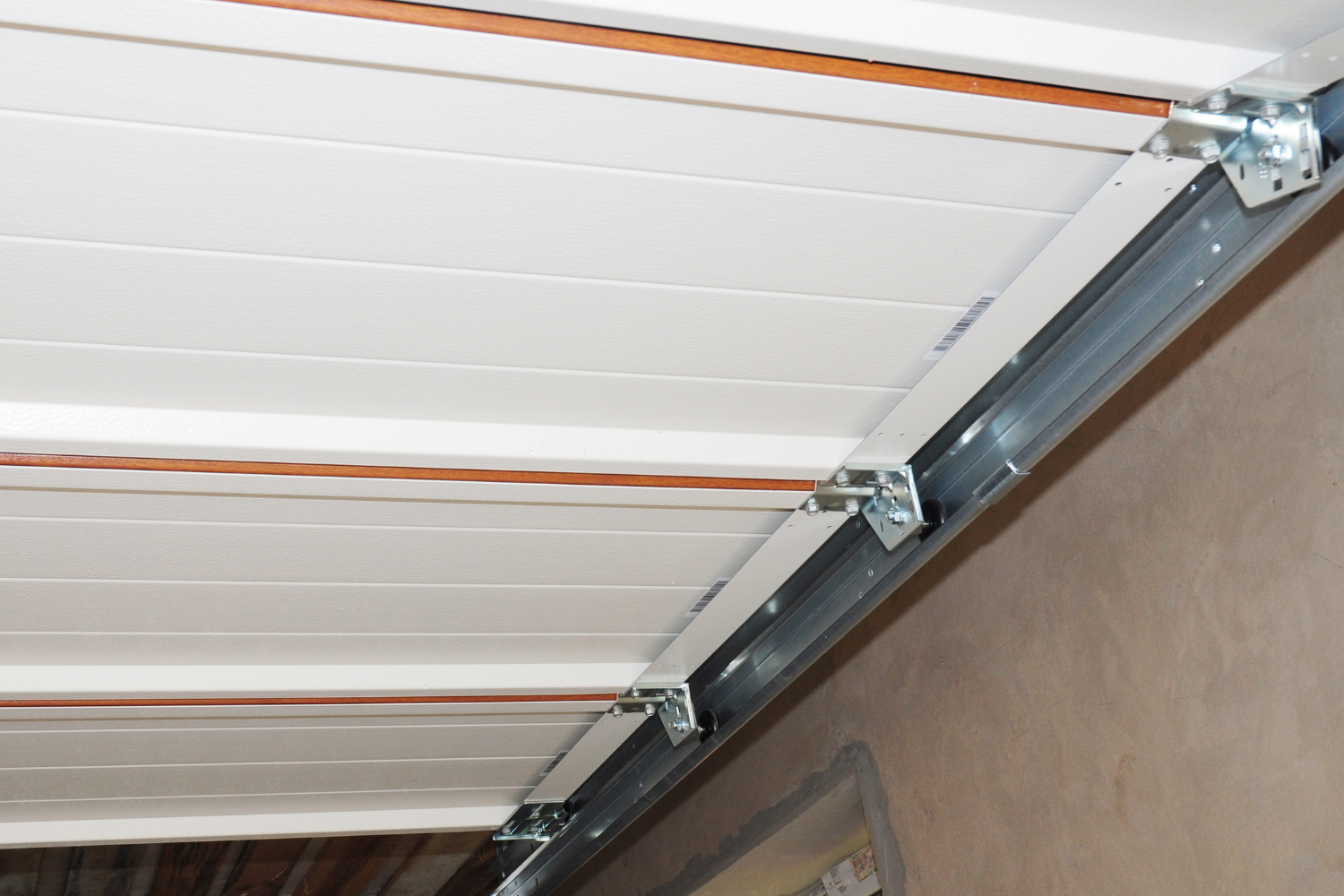Garage door track and brackets attached to the ceiling, white door panels, neutral setting.