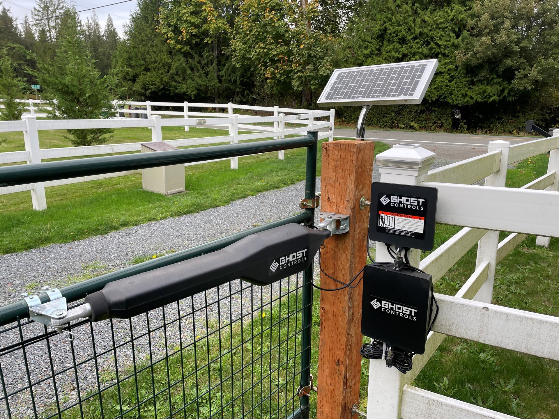Solar-powered automatic gate opener on a wooden post with control boxes and a solar panel.