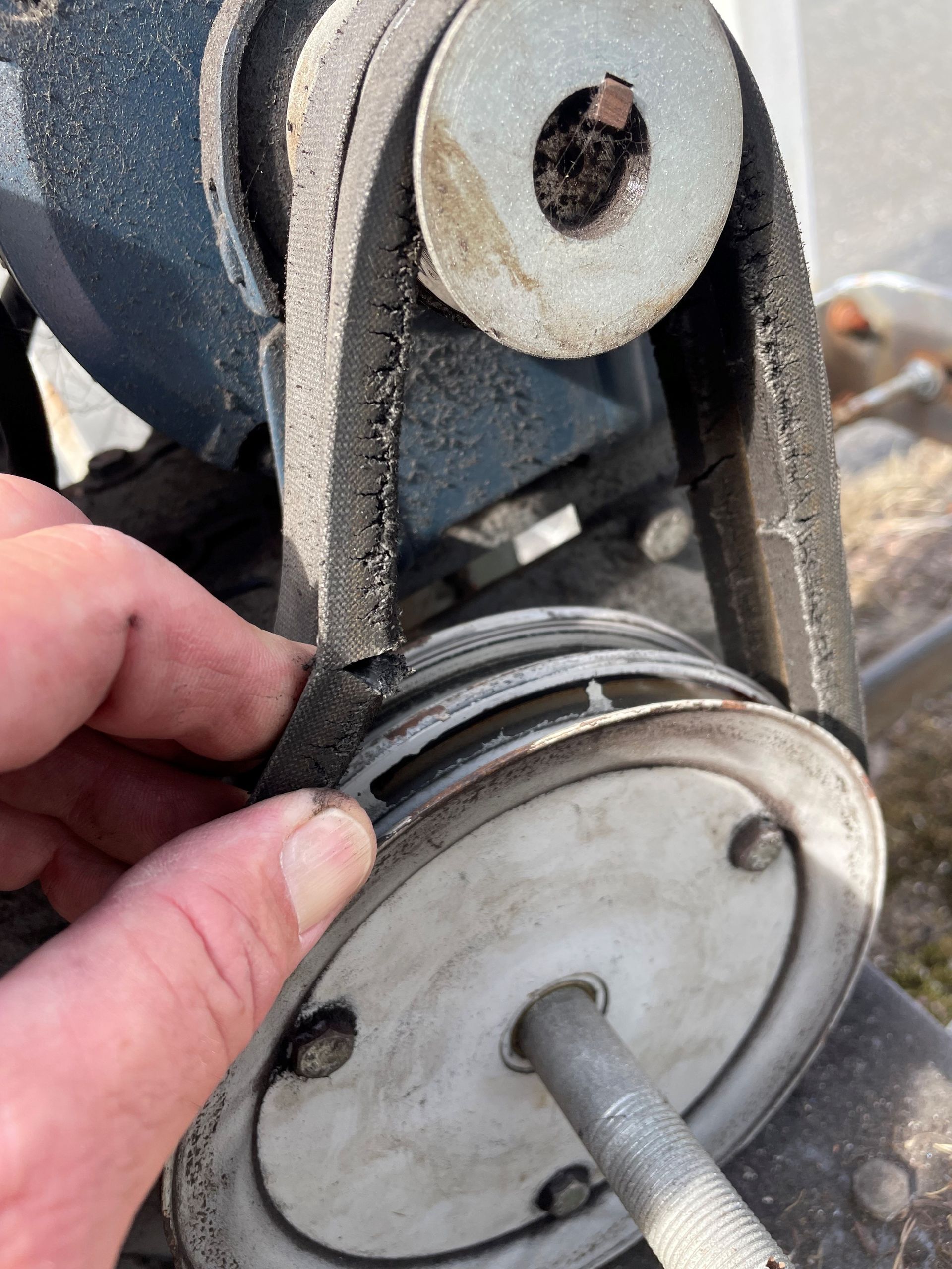Hand touching a worn V-belt on a pulley system, with a blue motor and dirty metal components.