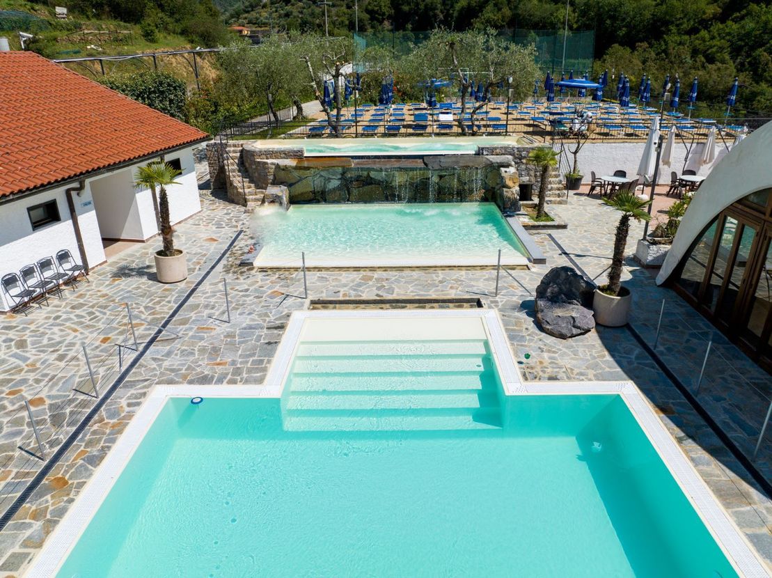 Cortile con piscina in stile resort, con vasche turchesi, patio in pietra e lettini prendisole.