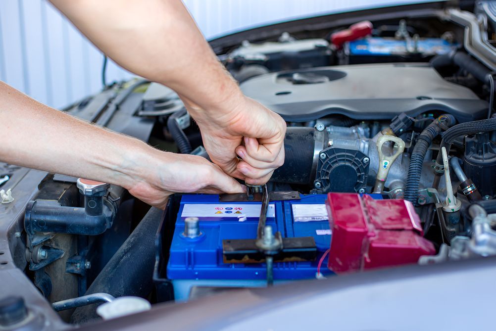 A Man is Fixing a Car Battery With a Wrench — Unified Mechanical – Mobile Mechanic In Byron Bay, NSW