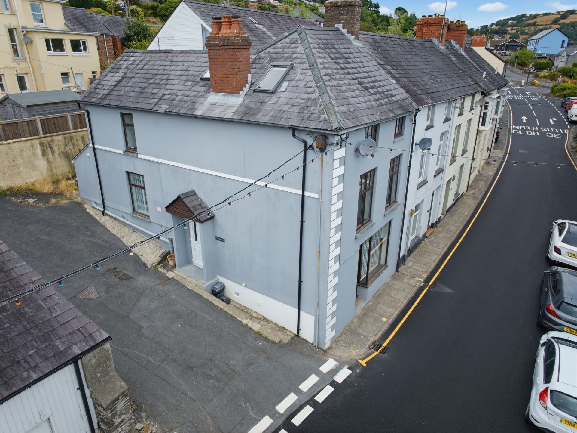 Aerial view of a white corner townhouse with gray slate roof on a street with parked cars.